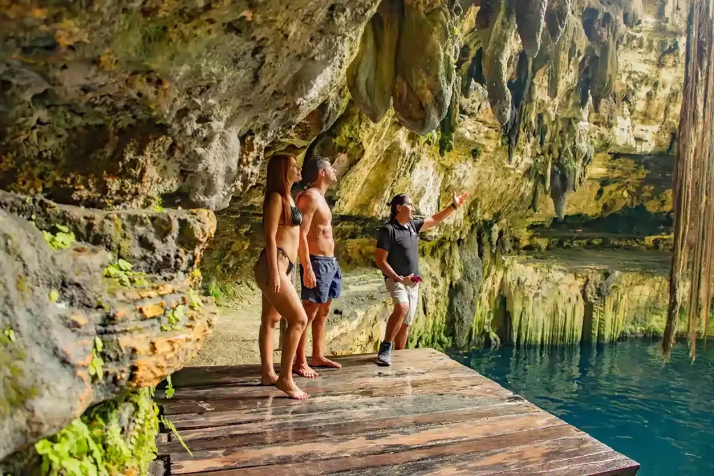A private tour guide explaining the history of the cenote to a couple of tourists inside a limestone cave in Yucatan.