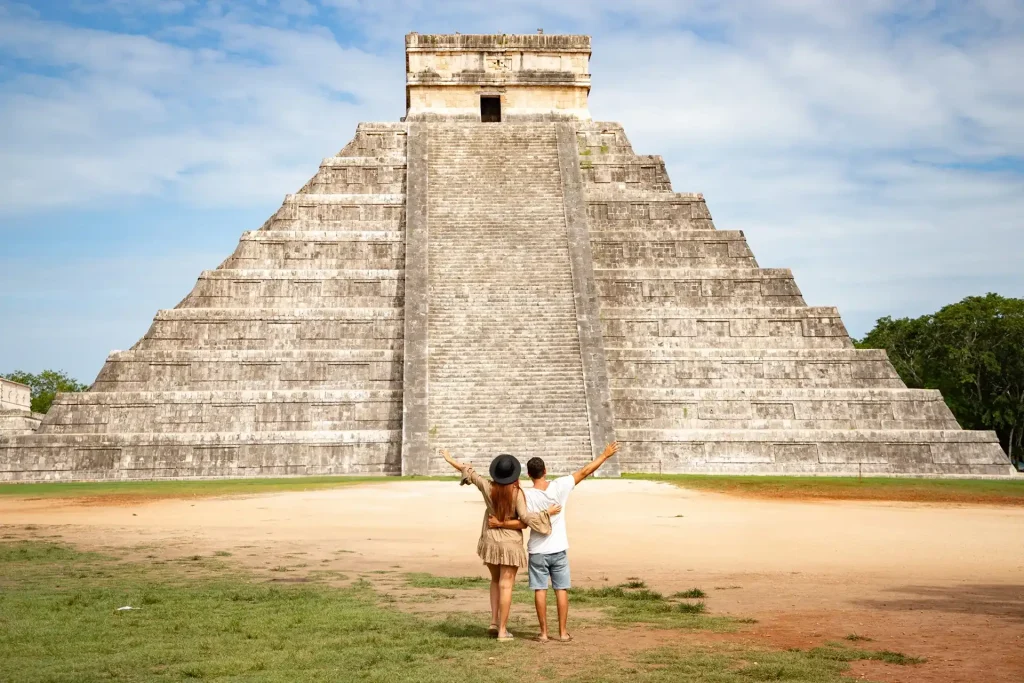 Couple with arms raised admiring El Castillo pyramid during a Chichen Itza private tour in Yucatán, Mexico.