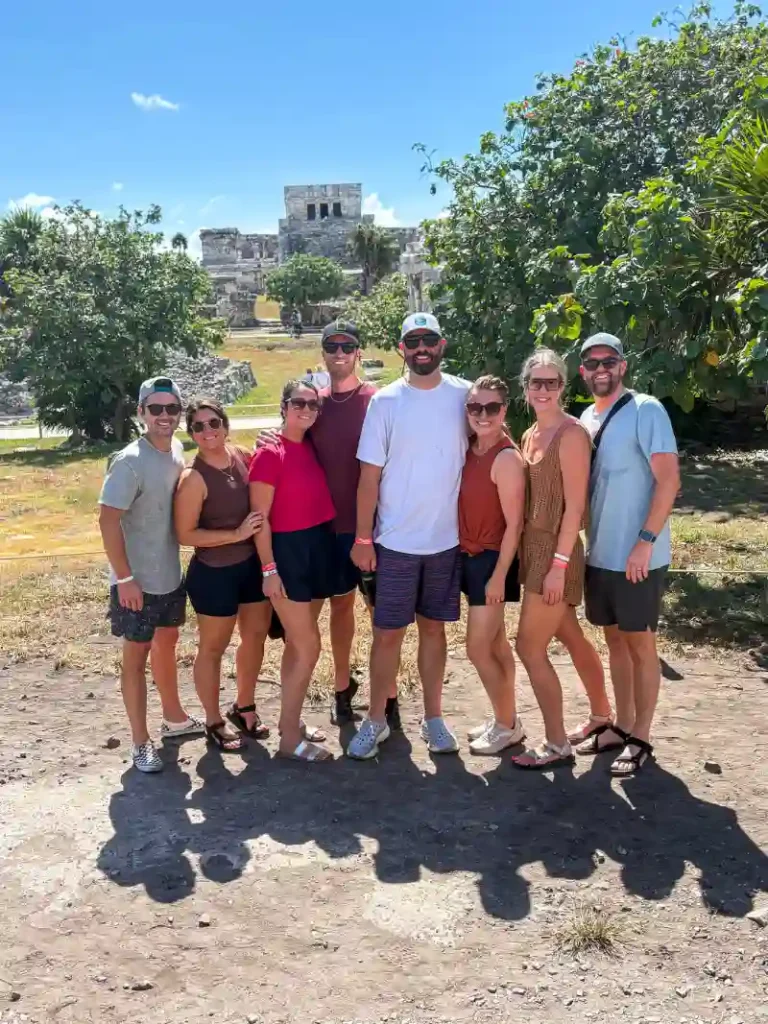 Group of friends posing together during a sunny private tour of the Tulum ruins, with ancient Mayan structures in the background.