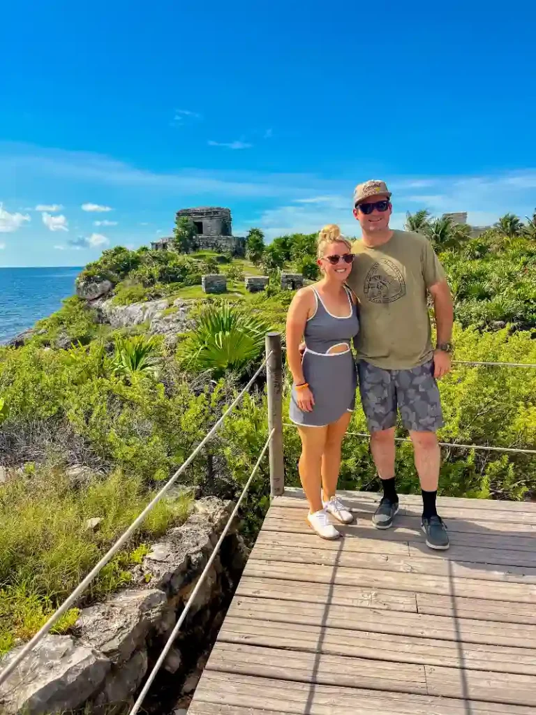 Smiling couple standing on a wooden platform overlooking the Tulum ruins during a private tour.