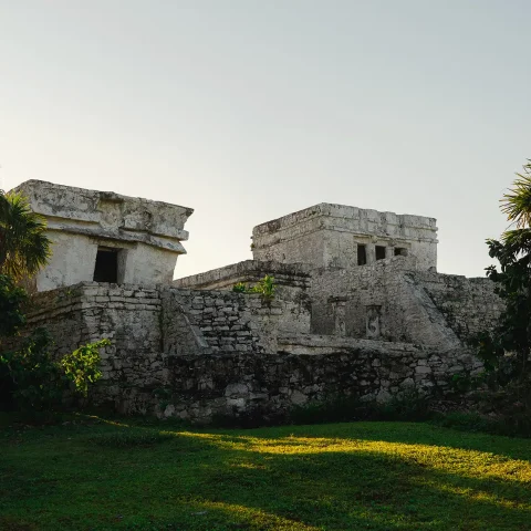 Ancient Mayan ruins at the Tulum archaeological site, surrounded by lush greenery and illuminated by soft sunlight.