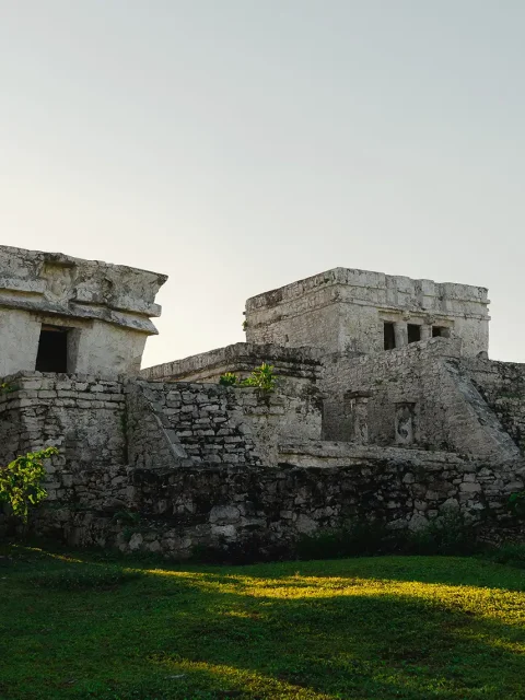 Ancient Mayan ruins at the Tulum archaeological site, surrounded by lush greenery and illuminated by soft sunlight.
