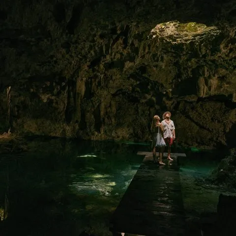 A young couple at one of the private cenote tour locations: a cave illuminated by dim light cascading from a ceiling hole.