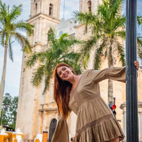 A young woman leaning on a lamppost, smiling next to the San Servacio Cathedral in Valladolid, Yucatan.