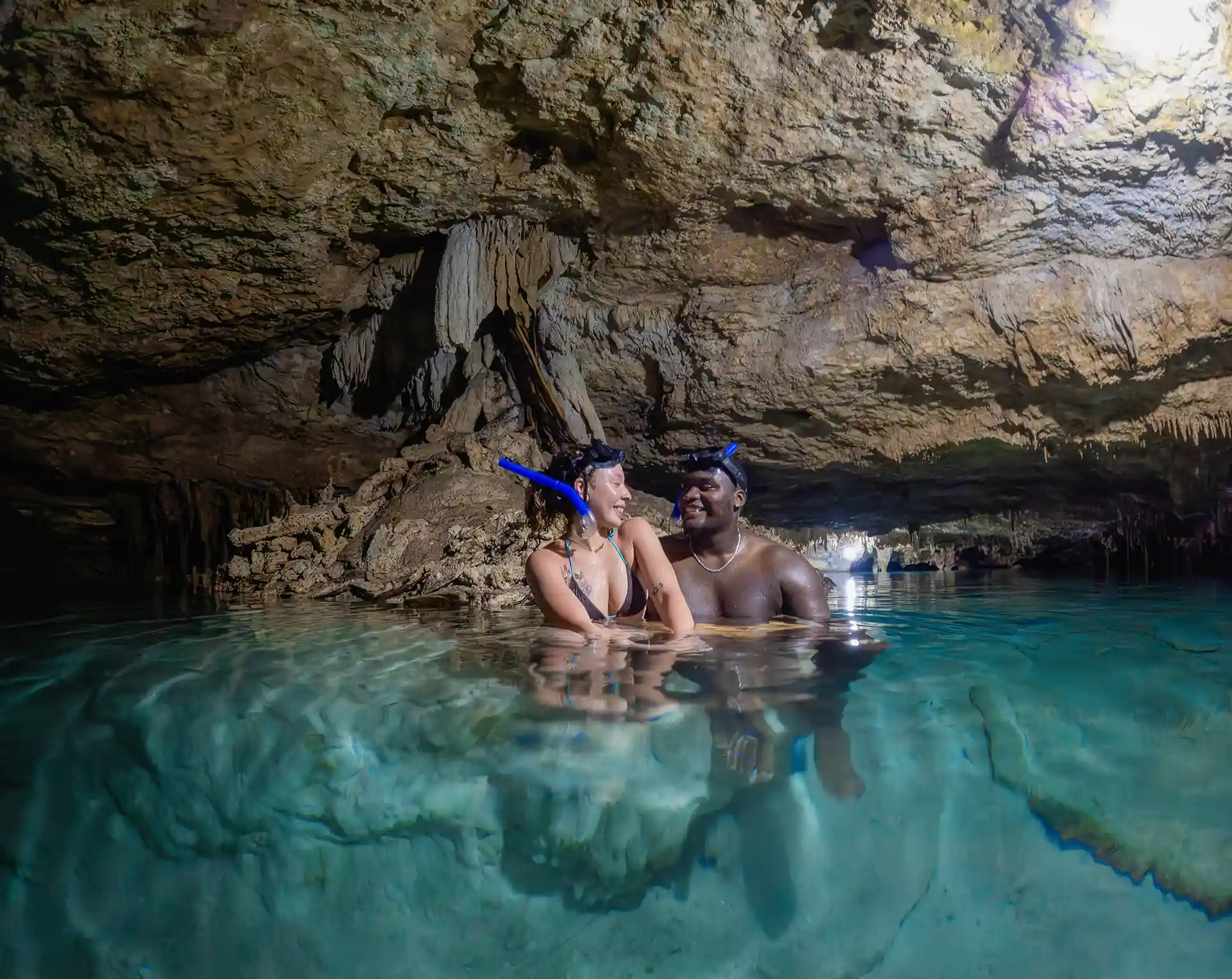 Couple enjoying a cenote tour in Tulum with snorkeling gear in a crystal-clear cave.