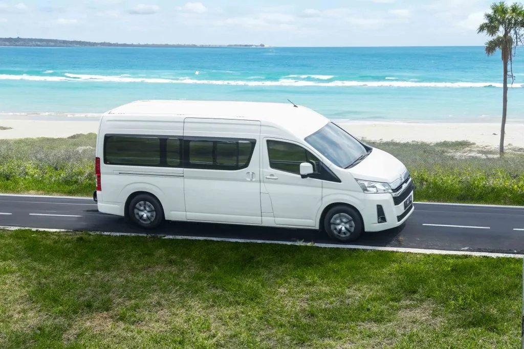 Toyota Hiace Van providing a Cancun to Tulum Private Transfer, driving alongside a scenic beach view.