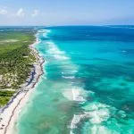 Aerial view of Tulum coast showcasing vibrant turquoise waters meeting the lush, dense jungle along the sandy shoreline.