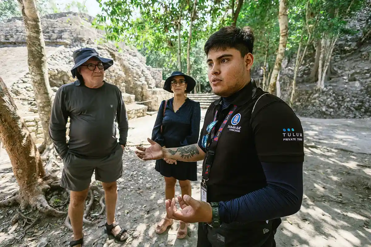 Tour guide leading a private tour with two tourists at the Coba ruins near Tulum, surrounded by ancient stone structures and dense jungle.