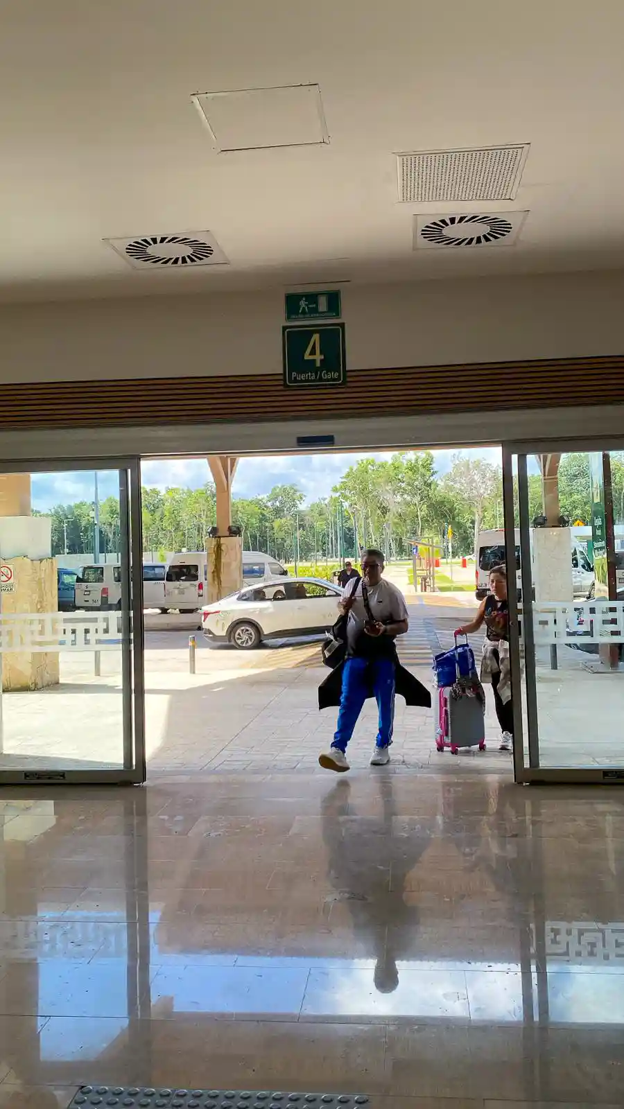 Travelers exiting through Gate 4 at Tulum International Airport, with luggage in hand and transport vehicles waiting outside.