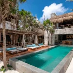 Luxury beachfront villa in Tulum with private pool, wooden lounge chairs, palm trees, and rustic-chic architecture blending with tropical surroundings.