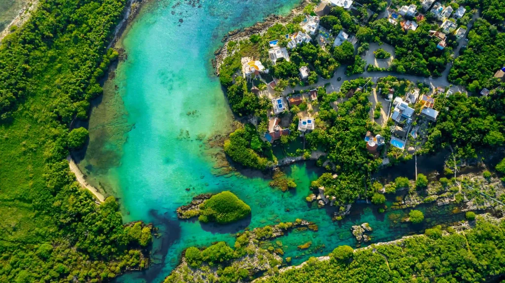 Drone view of Yal Ku Lagoon, showcasing its turquoise waters surrounded by lush jungle, with the ocean seamlessly connecting to the lagoon.