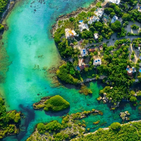 Drone view of Yal Ku Lagoon, showcasing its turquoise waters surrounded by lush jungle, with the ocean seamlessly connecting to the lagoon.