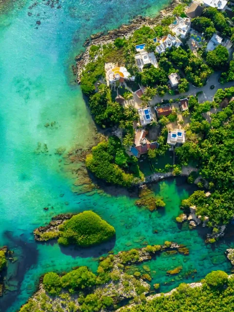 Drone view of Yal Ku Lagoon, showcasing its turquoise waters surrounded by lush jungle, with the ocean seamlessly connecting to the lagoon.
