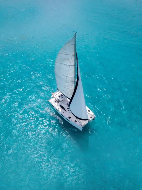 Aerial view of a catamaran sailing through the crystal-clear waters of Cancun's Caribbean Sea.