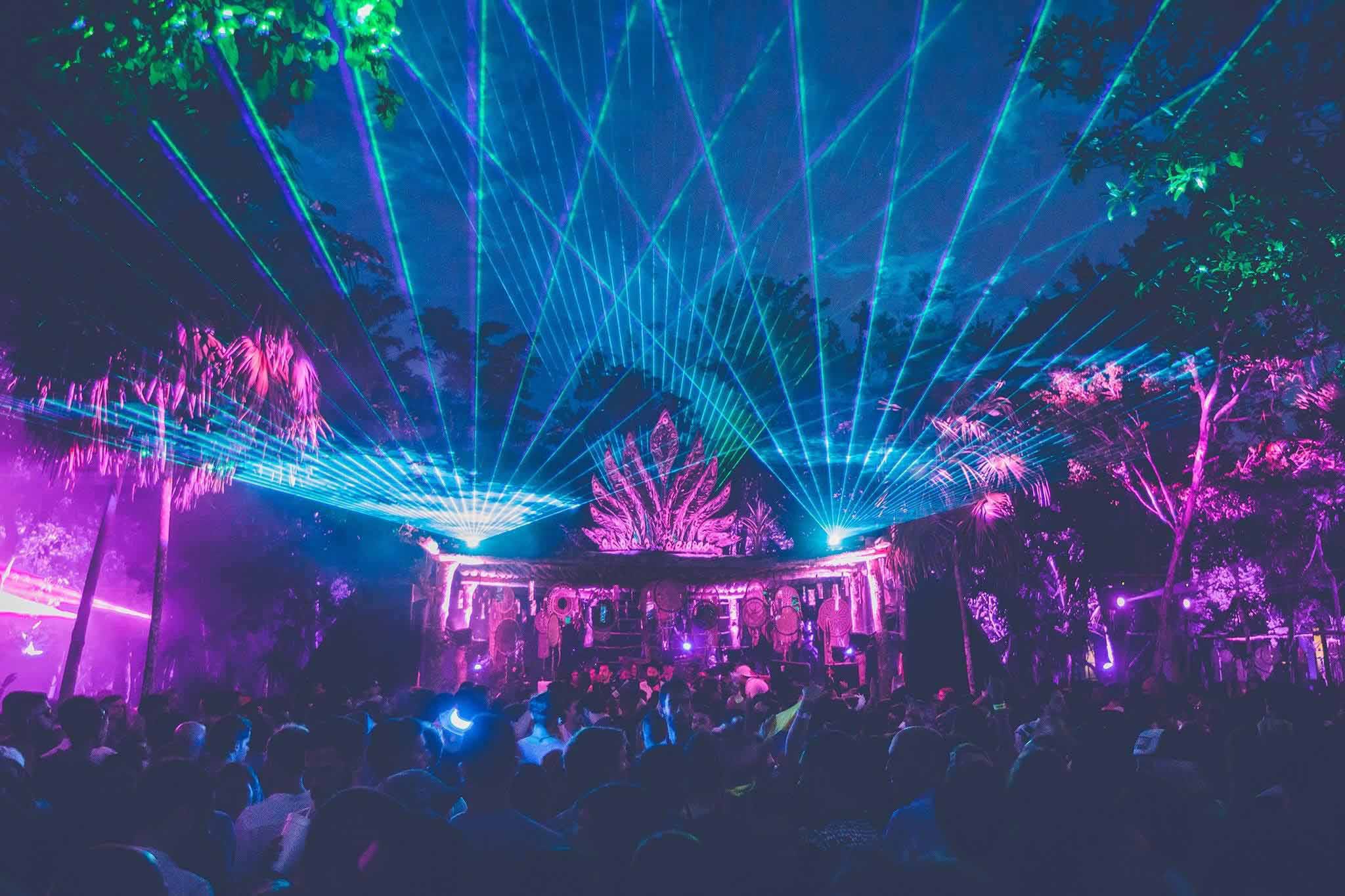 Electronic music event in the Tulum jungle with vibrant lights and dancing crowd