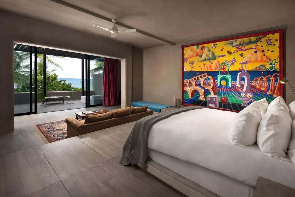 Luxury hotel boutique in Tulum with modern bedroom, colorful mural, ocean-view balcony, and cozy seating area.