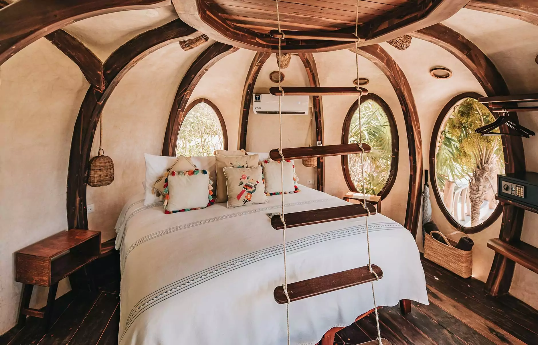 Interior of a unique eco-friendly treehouse room in Tulum with wood beams, oval windows, and rustic decor.