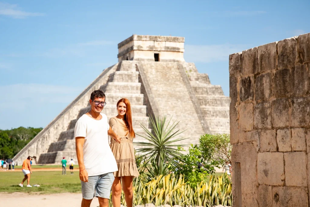 Smiling couple touring the historic site of Chichen Itza, with the iconic Kukulcan pyramid visible.