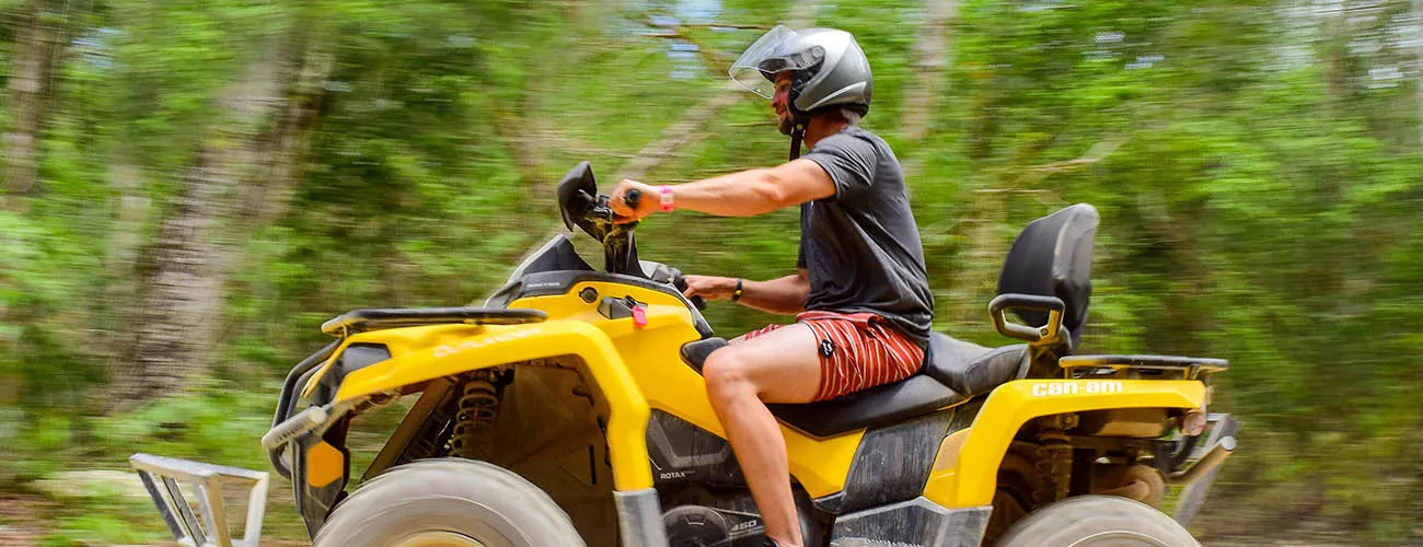 Man riding a yellow Can-Am ATV through a lush jungle trail in Tulum.