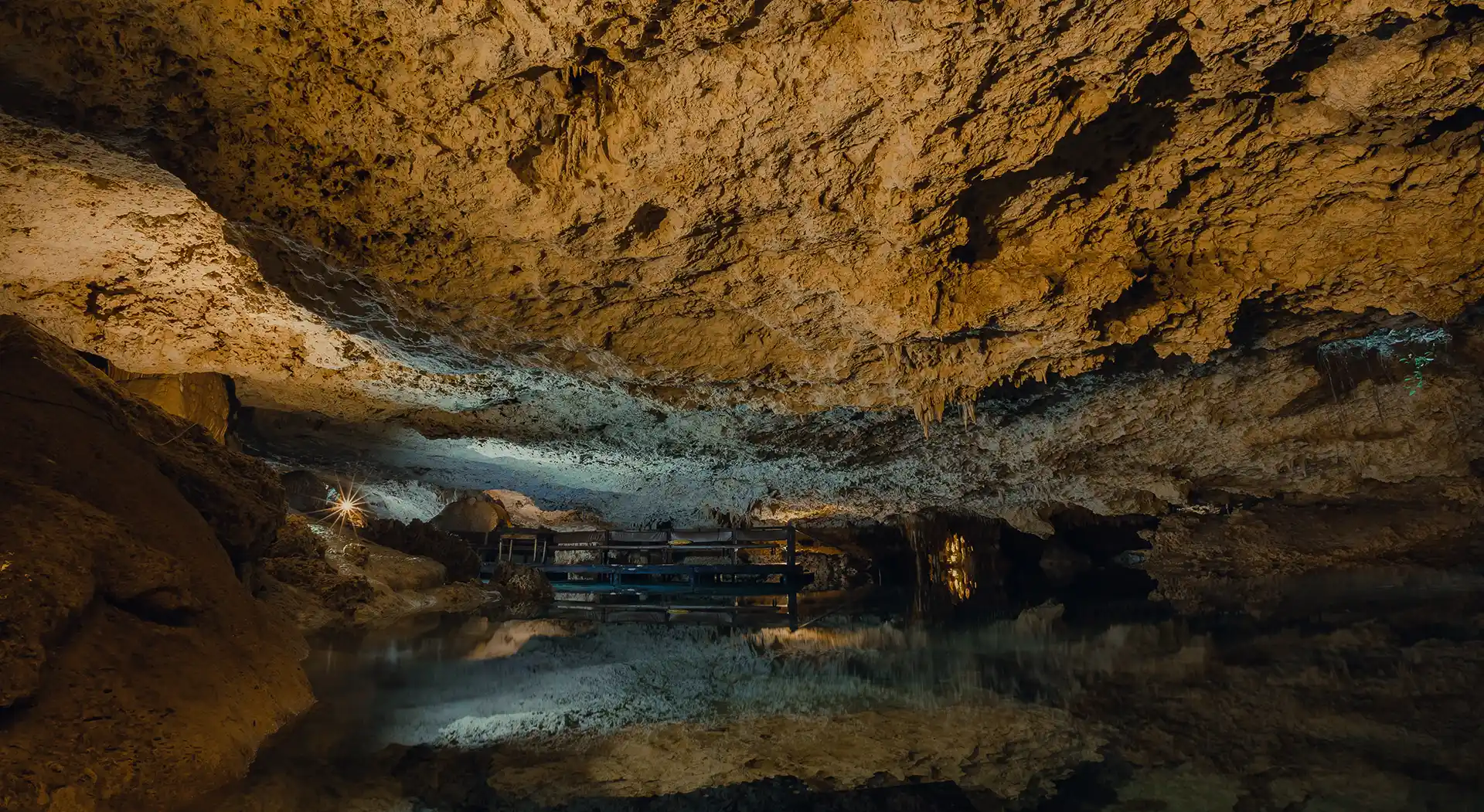 “Underground cave with clear turquoise water and dramatic stalactites hanging from the ceiling.