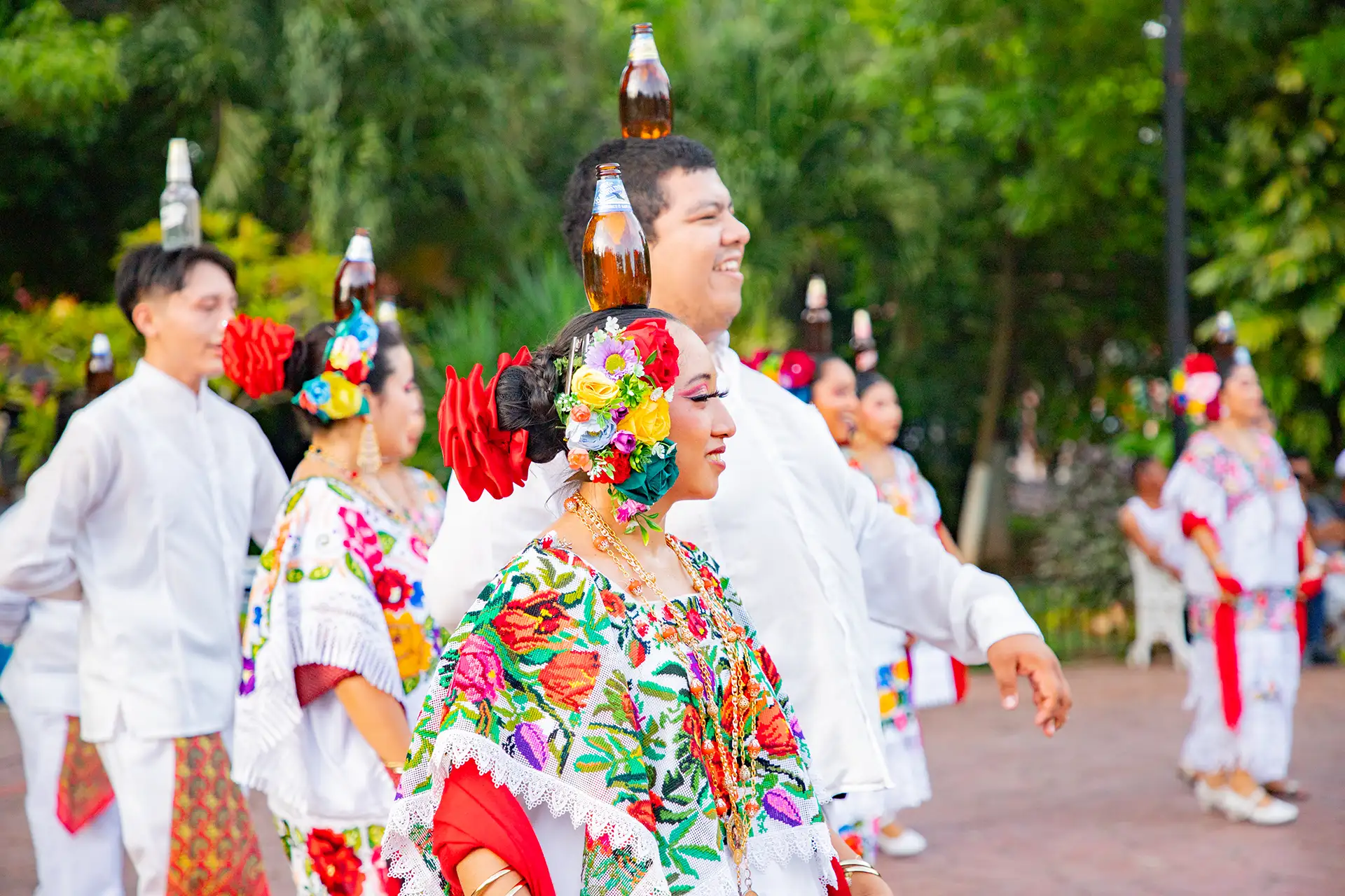 Traditional folkloric dancers in Valladolid wearing vibrant, embroidered attire, balance bottles on their heads while gracefully performing.