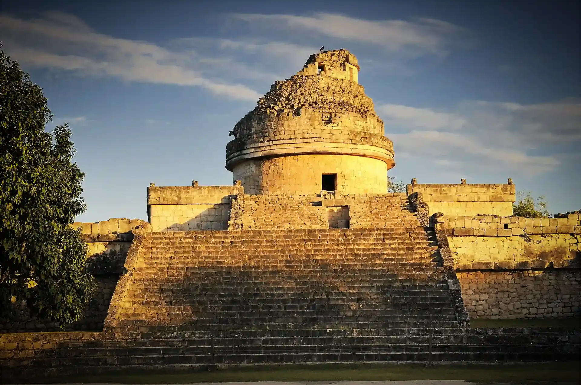 A vibrant turquoise ocean meets a sandy beach below a rocky cliff covered in lush green vegetation in beautiful Tulum, Mexico.