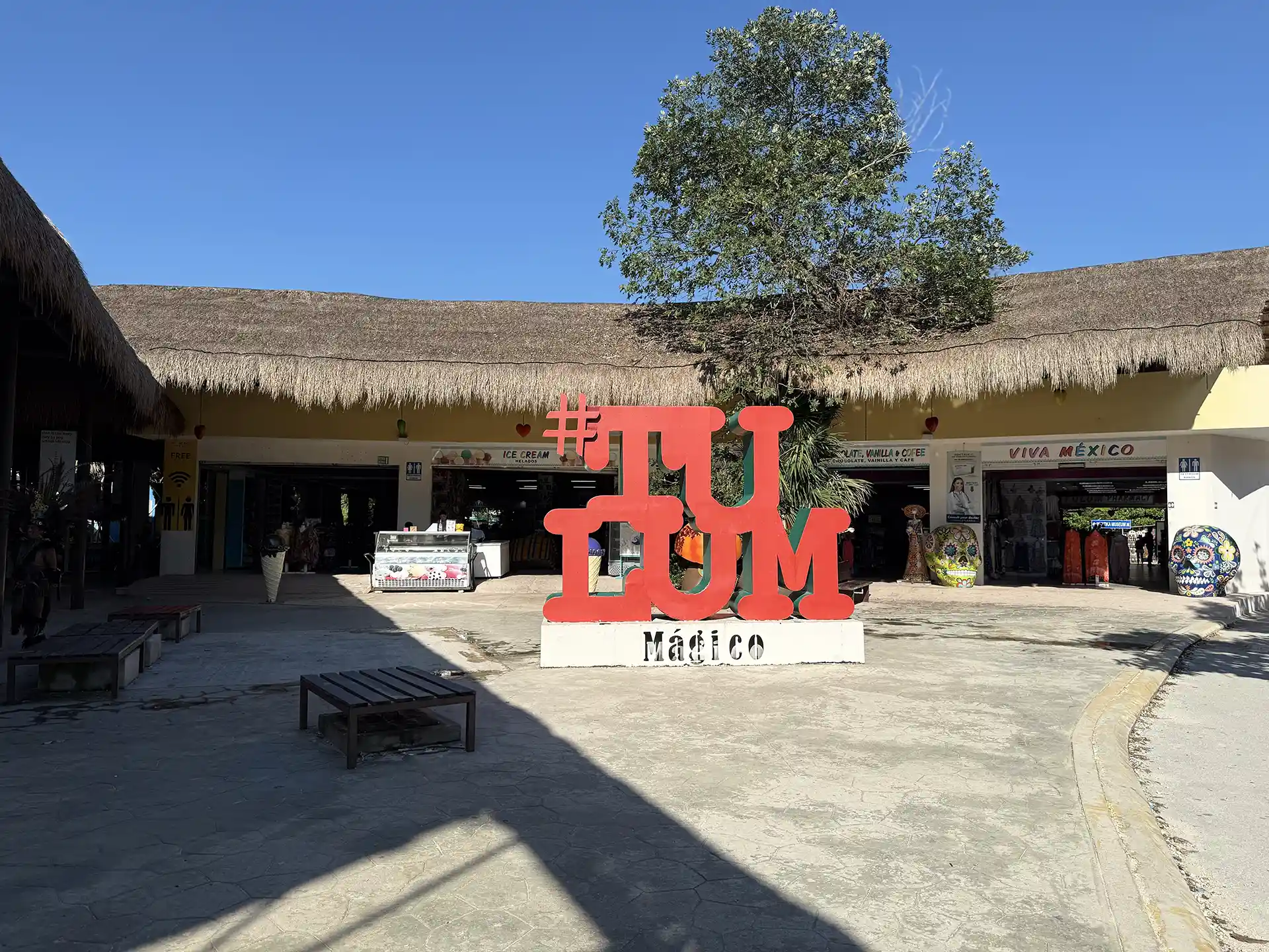 Tulum souvenir shops with a thatched-roof marketplace featuring a large red #Tulum sign, local crafts, and traditional decor.