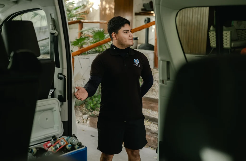 A private driver in uniform stands beside a well-equipped transport van, ready to assist travelers heading to Chichén Itzá, offering personalized service and convenience.