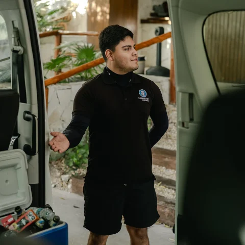 A private driver in uniform stands beside a well-equipped transport van, ready to assist travelers heading to Chichén Itzá, offering personalized service and convenience.