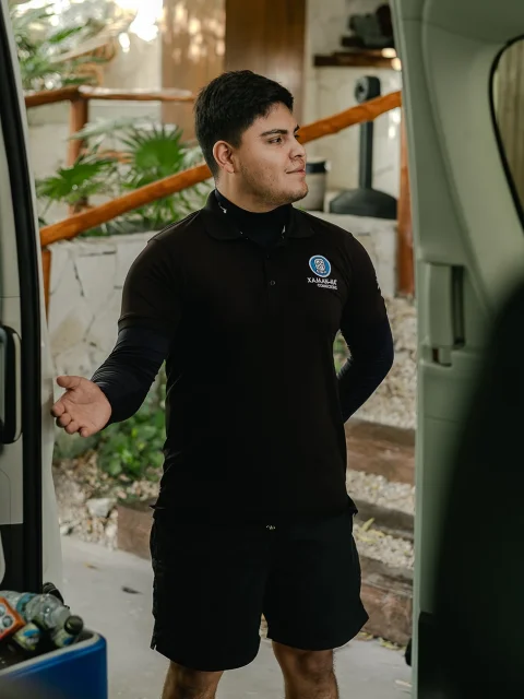 A private driver in uniform stands beside a well-equipped transport van, ready to assist travelers heading to Chichén Itzá, offering personalized service and convenience.