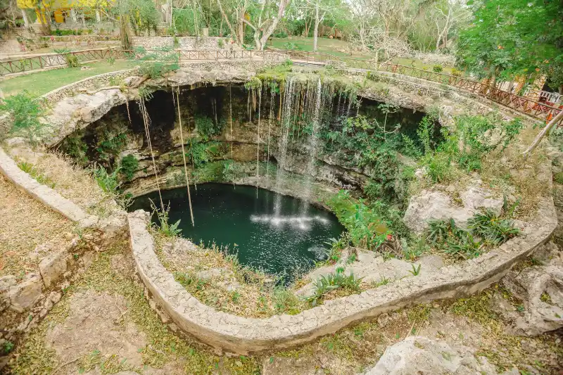 Cenote Saamal open-air sinkhole with turquoise water and waterfall.