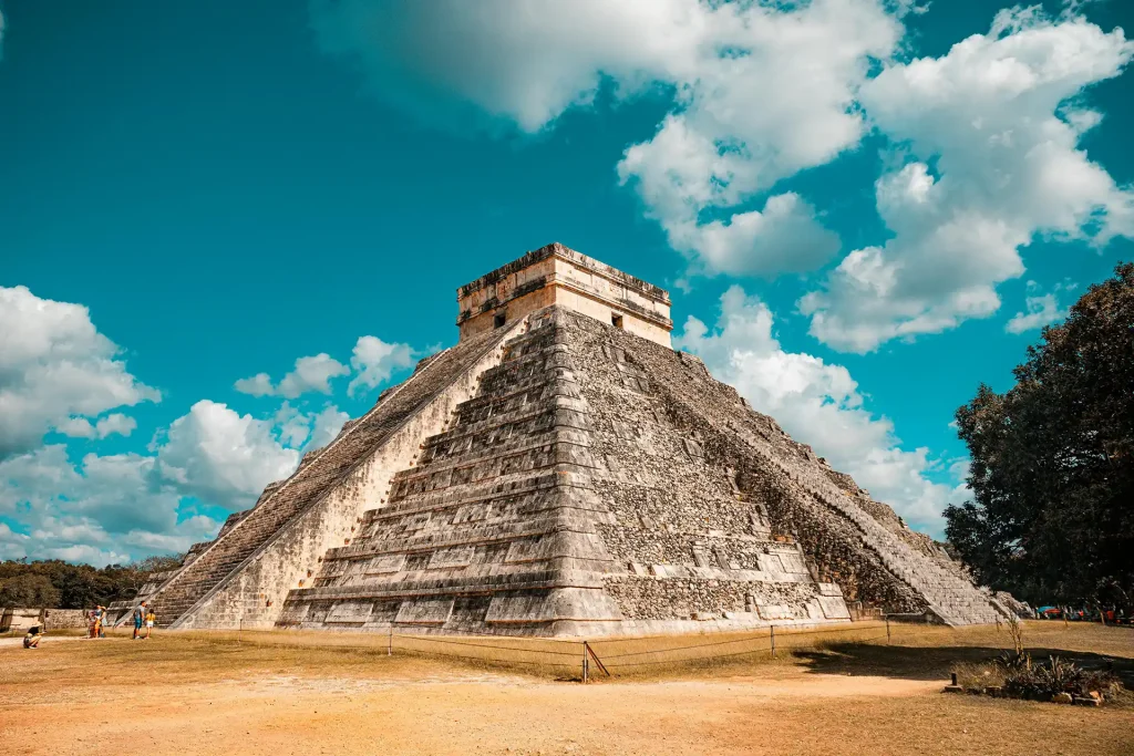 The iconic El Castillo pyramid at Chichen Itza in Yucatan, Mexico, standing tall under a vibrant blue sky with scattered clouds.