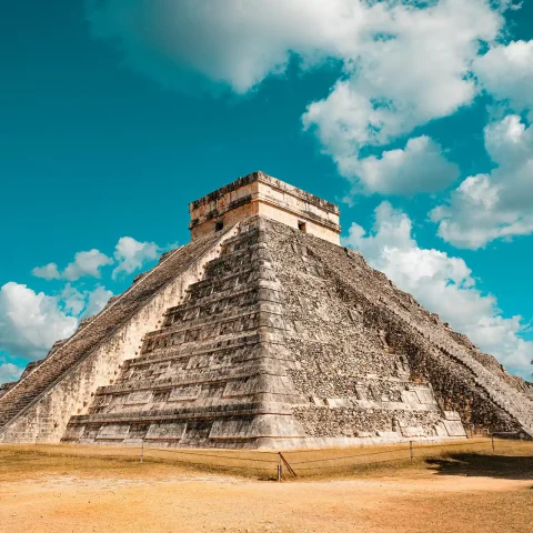 The iconic El Castillo pyramid at Chichen Itza in Yucatan, Mexico, standing tall under a vibrant blue sky with scattered clouds.