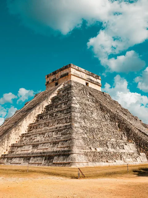 The iconic El Castillo pyramid at Chichen Itza in Yucatan, Mexico, standing tall under a vibrant blue sky with scattered clouds.