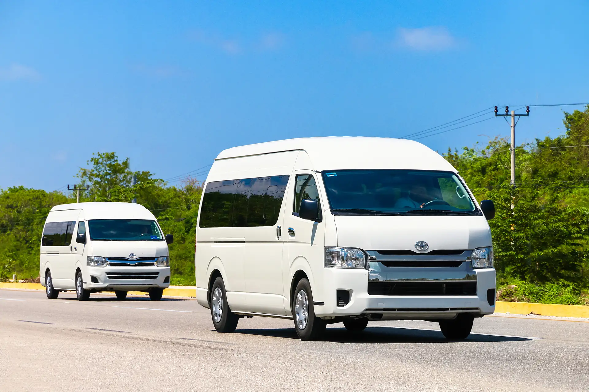 Two white Toyota vans drive along a sunny highway, ideal for promoting group transportation services for tours in Tulum.