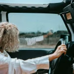 Woman driving a Jeep with the top down on a rural road.