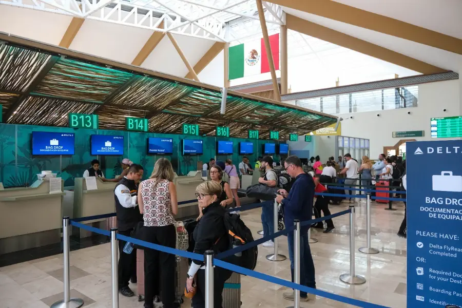 Travelers checking in at TQO International Airport terminal with the Mexican flag visible overhead.