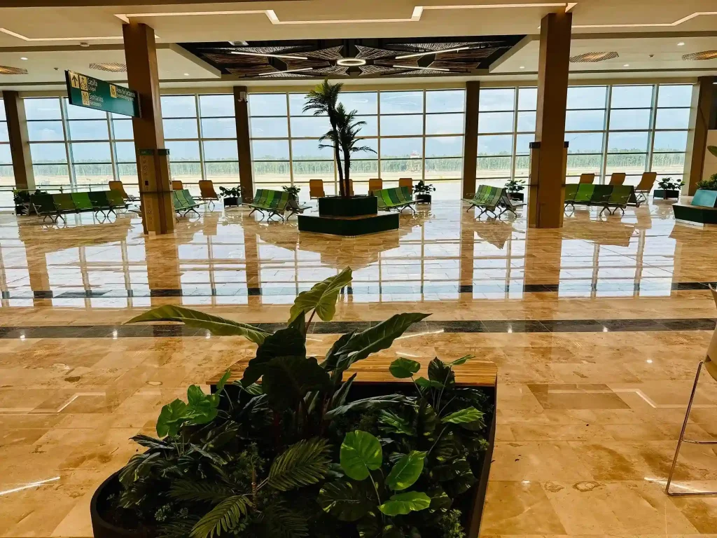 Spacious interior of Tulum Airport terminal with modern seating, large windows, and tropical plants.