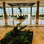 Spacious interior of Tulum Airport terminal with modern seating, large windows, and tropical plants.