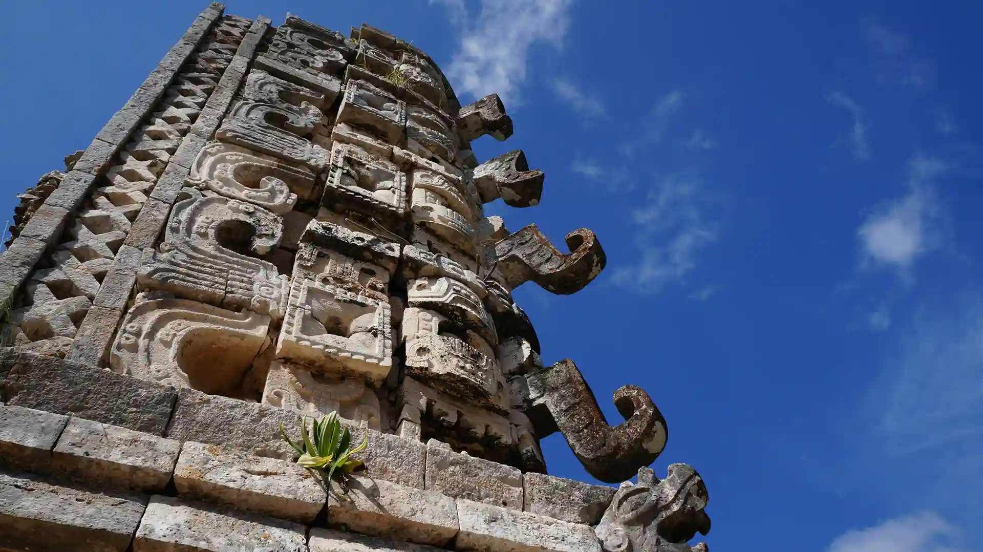 Close-up view of intricate Mayan carvings and decorative stonework on a temple at Uxmal against a clear blue sky