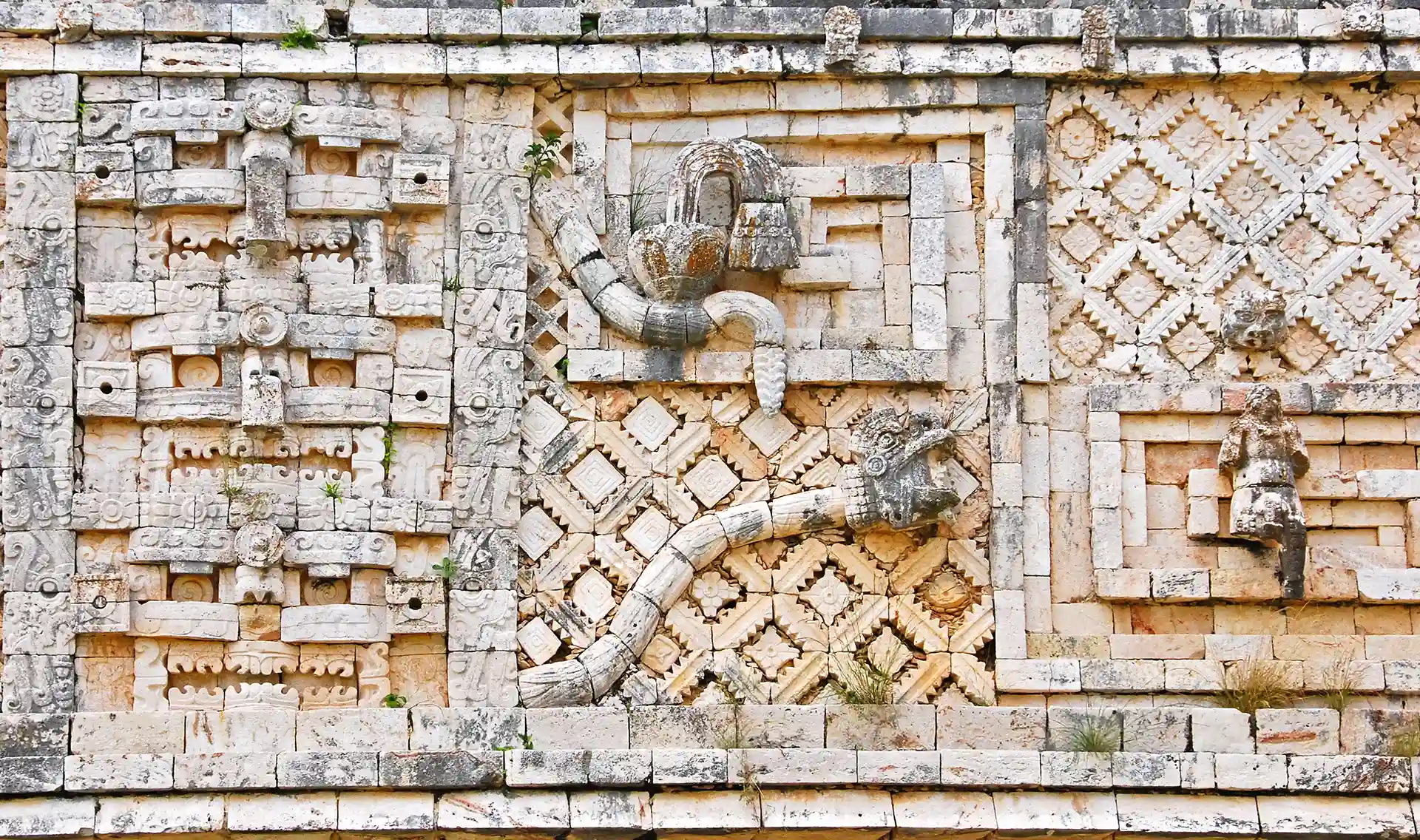 Close-up of intricate Mayan carvings on a stone wall at Uxmal, featuring symbolic patterns and serpent motifs