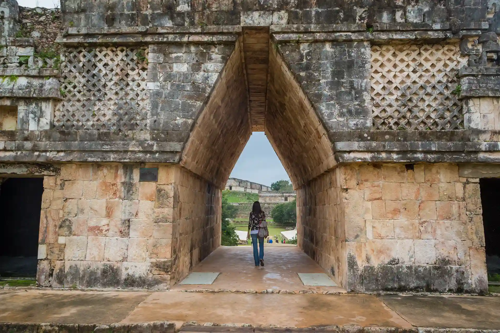 Person walking through a triangular stone archway at the ancient Mayan city of Uxmal.
