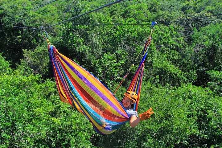 Woman zip lining through the Tulum jungle in a colorful hammock with safety gear.