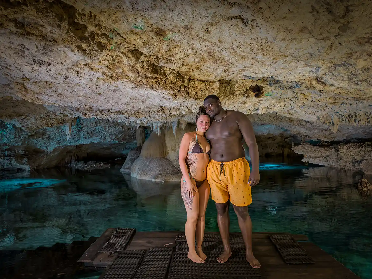 Couple standing on a wooden deck inside a scenic underground cenote.