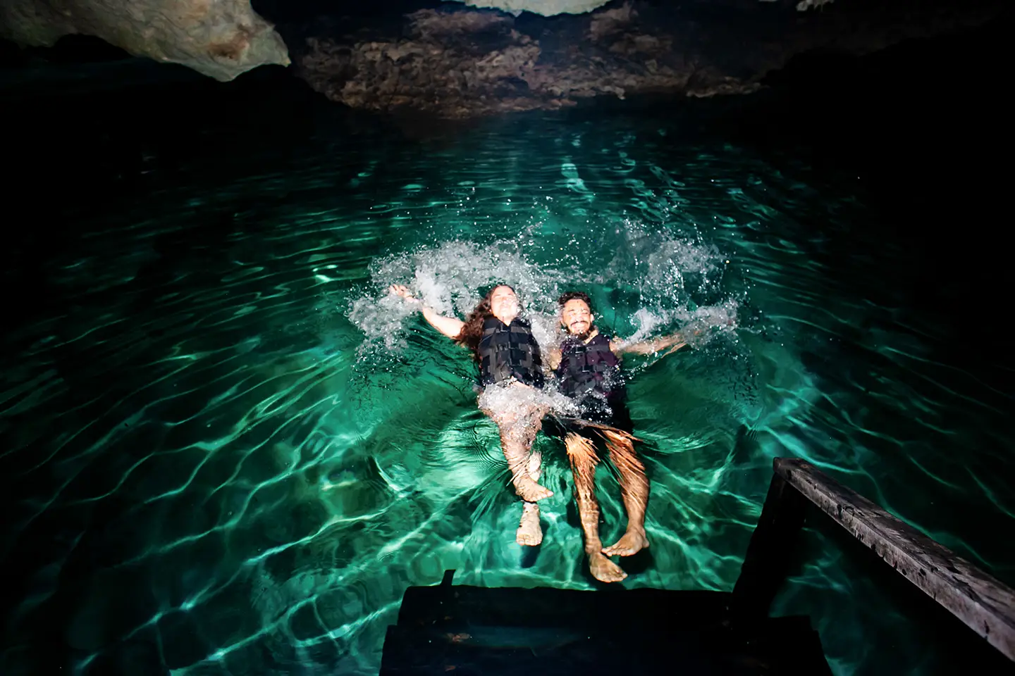 Couple wearing life vests splashing in a crystal-clear underground cenote in Riviera Maya.