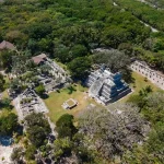 Aerial view of El Meco Mayan ruins near Cancún, featuring a central stepped pyramid surrounded by lush jungle and smaller stone structures.