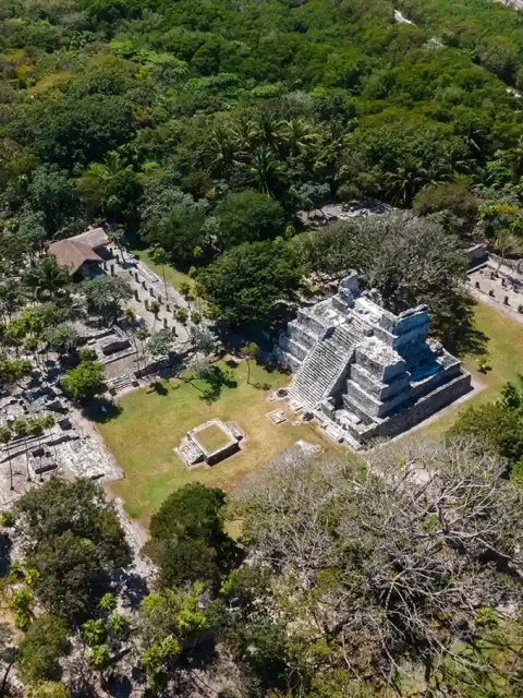 Aerial view of El Meco Mayan ruins near Cancún, featuring a central stepped pyramid surrounded by lush jungle and smaller stone structures.