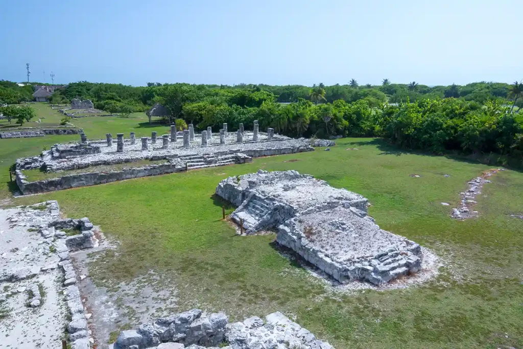 El Rey Mayan ruins in Cancún showcasing stone platforms, columns, and grassy open areas surrounded by dense tropical vegetation.