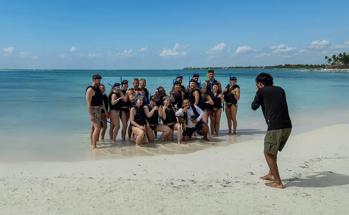 Group of tourists in snorkel gear posing for a photo on a tropical beach, guided by a Xaman-Ha Connections tour photographer.