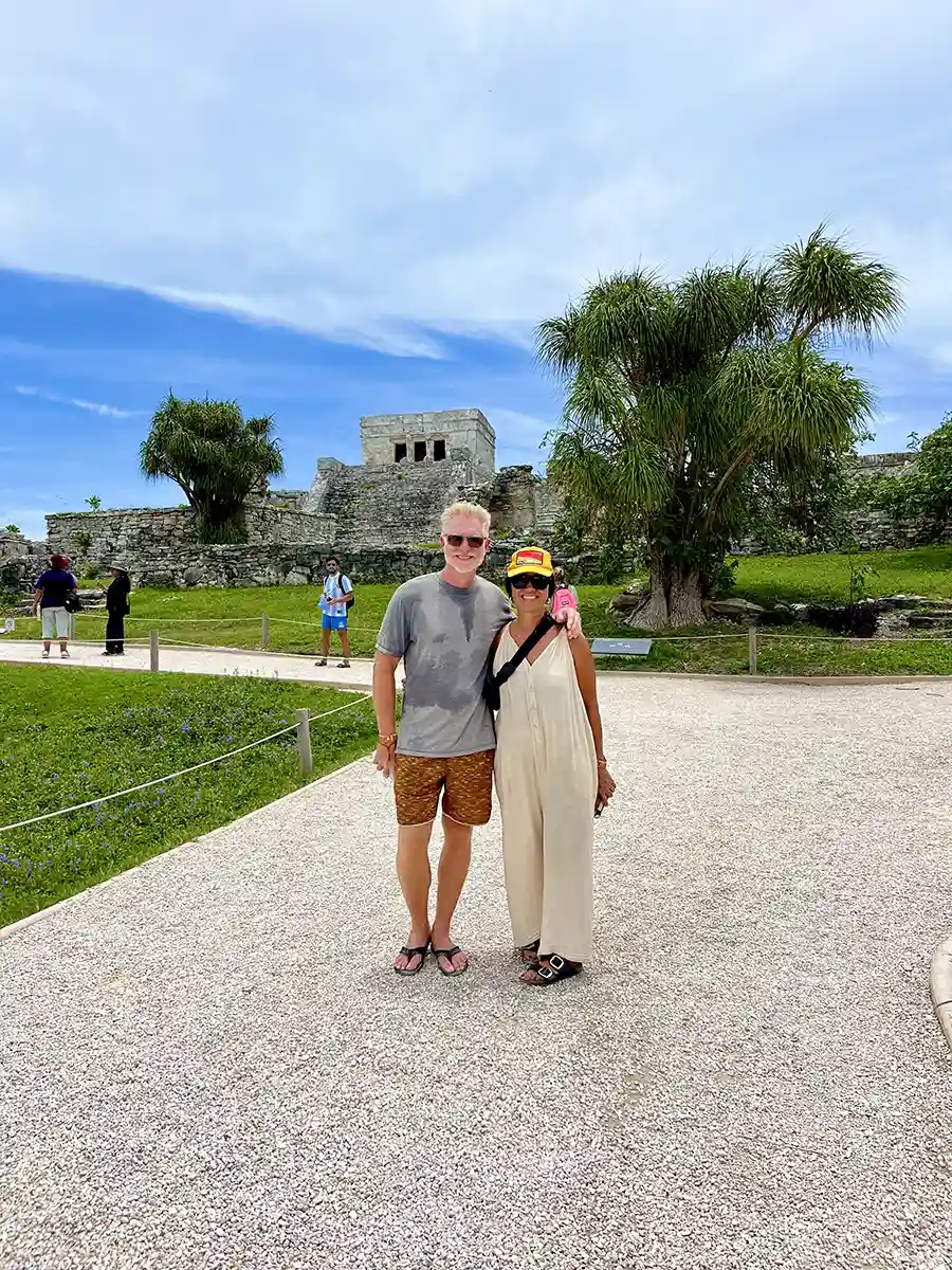 Couple standing in front of Tulum Mayan Ruins with visible in the background.